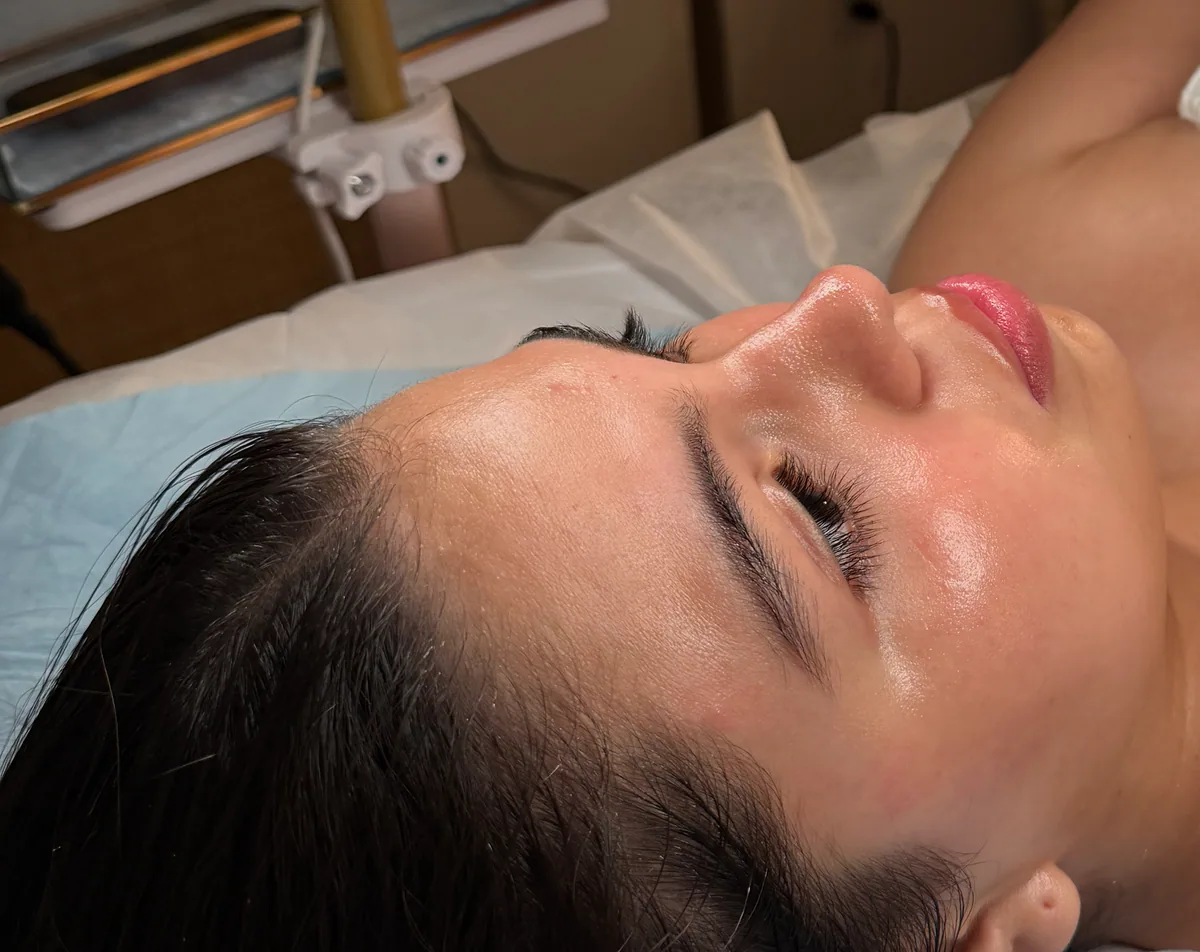 A client relaxing during a skincare appointment under a magnifying lamp.