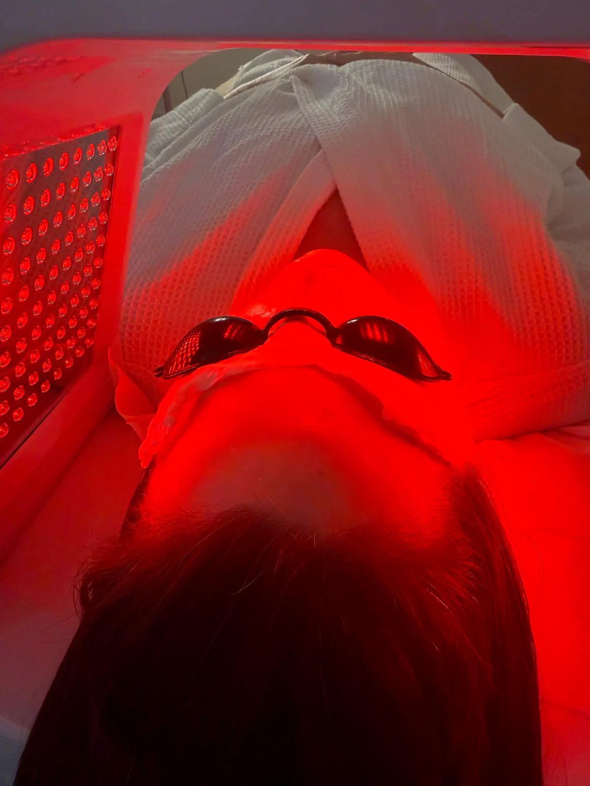 A client resting under red LED light during a skincare treatment.